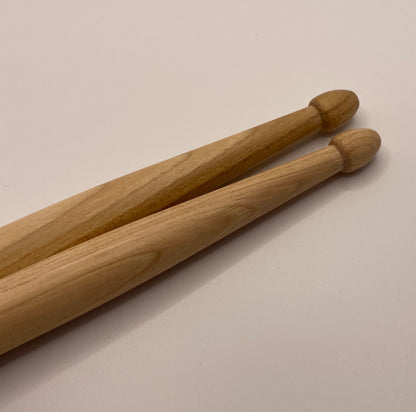 Two wooden drumsticks on a beige background with Acorn tips