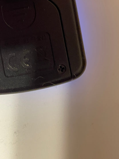 Close-up of a black guitar tuner corner showing battery case security screw installation on a light background