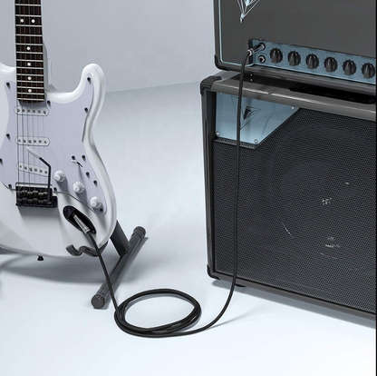 White electric guitar on a stand connected to a black amplifier with a white background